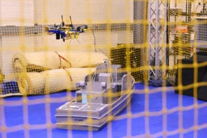 An unmanned system maneuvers over a scale model of a U.S. Navy Yard Patrol craft inside an indoor flight testing facility at the Naval Air Warfare Center Aircraft Division (NAWCAD). The controlled testing environment allows engineers to validate computer vision and flight control algorithms that track relative ship movement before taking the software to live-flight sea trials. (Photo: U.S. Navy by Chuck Regner)